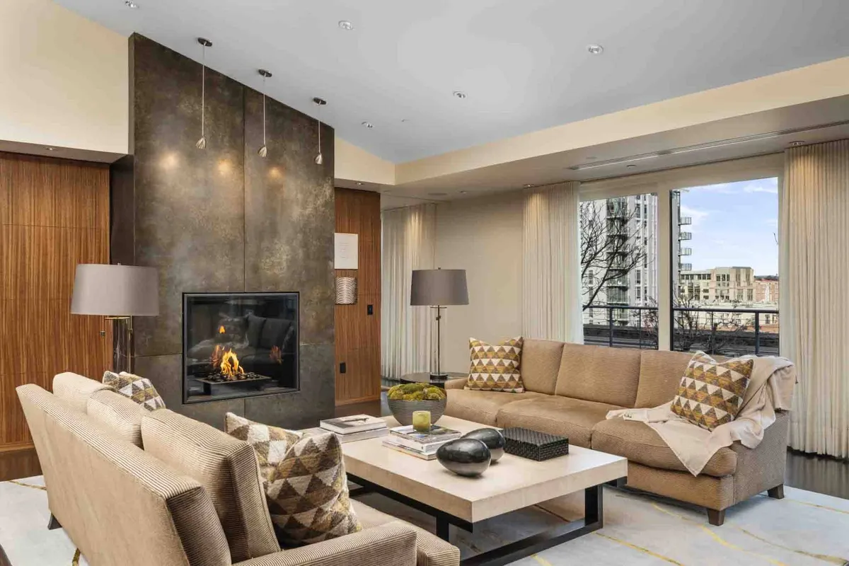 A cozy, contemporary living space with a modern fireplace, a comfortable sofa, a coffee table, and large windows that let in abundant natural light and offer glimpses of the city outside. The setup is perfect for socializing, unwinding, or reading after a day of adventures.