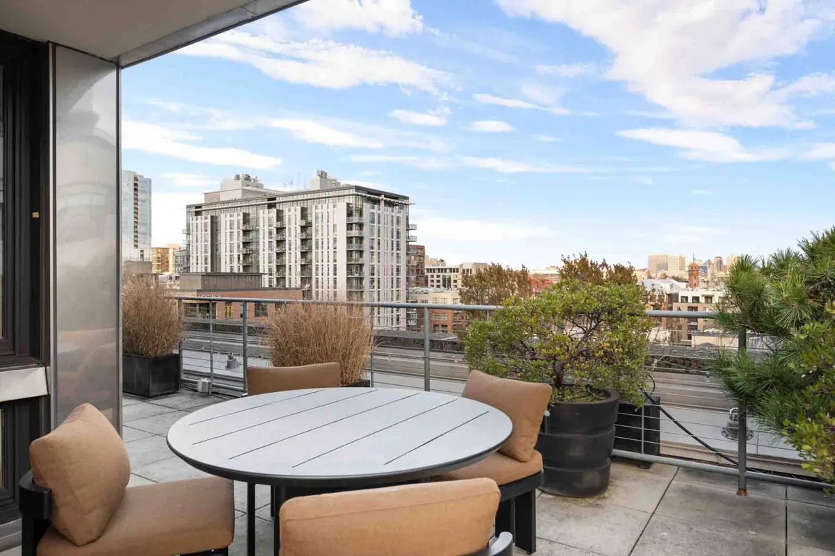 A contemporary terrace setup featuring a circular table with surrounding chairs, planters, and striking views of the city skyline. This inviting space is ideal for outdoor dining, entertaining, or simply enjoying the sweeping three-sided exposure the terrace offers.
