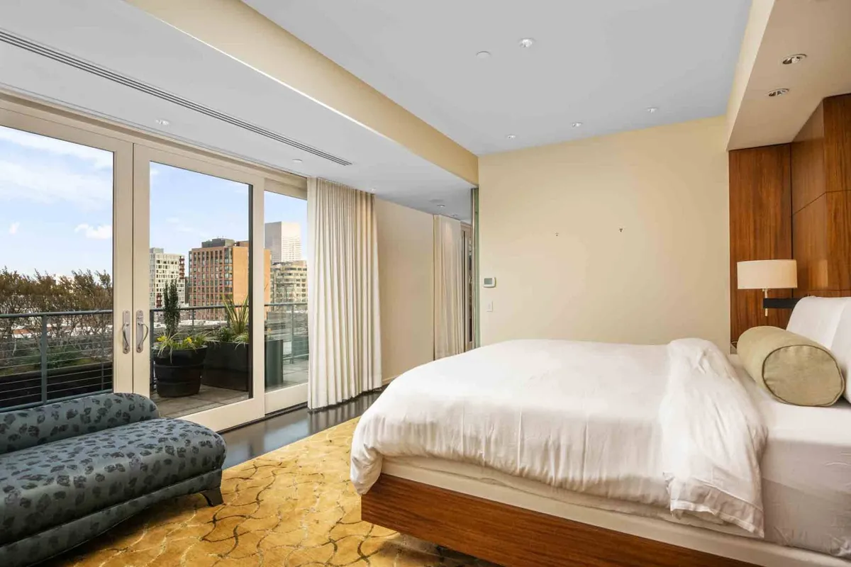 This image showcases a serene, contemporary living and sleeping area with large windows offering expansive city views. The bed and sofa are positioned to enjoy natural light and the urban landscape, suggesting a seamless connection between interior comfort and the bustling city beyond.