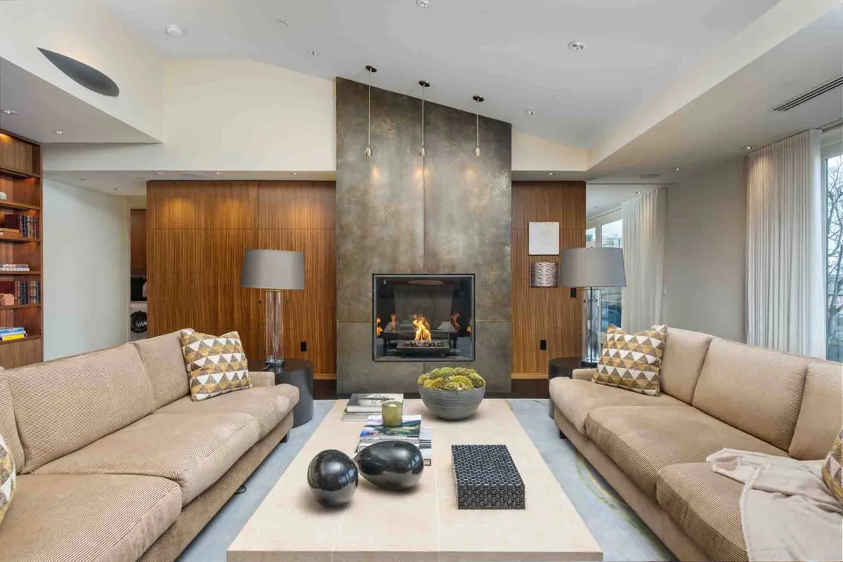 A warm and inviting living room centered on a stylish fireplace, surrounded by comfortable sofas with patterned cushions and a coffee table, all set beneath large windows that invite light and views.