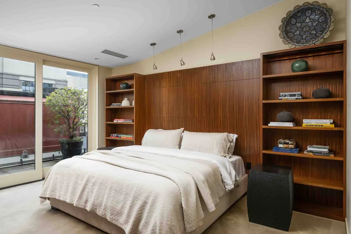 A cozy, modern bedroom featuring a bed, bookshelves, and a large window that frames the city below. The space is designed for relaxation, with abundant natural light and a calming atmosphere that invites unwinding after a day of city exploration.